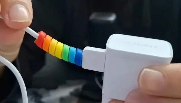Cabo de carregador branco com um protetor em espiral de silicone colorido em tons de arco-íris (laranja, amarelo, verde e azul) aplicado na base próxima ao conector.