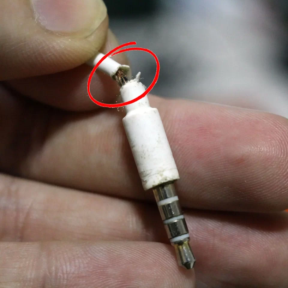 Close-up de um conector de fone de ouvido branco com o cabo visivelmente partido e fios expostos próximo à base do plugue.