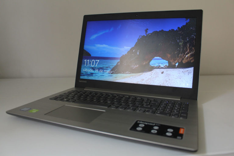 Notebook Lenovo IdeaPad 320 cinza aberto sobre uma mesa, mostrando a tela com papel de parede de paisagem e o teclado numérico.