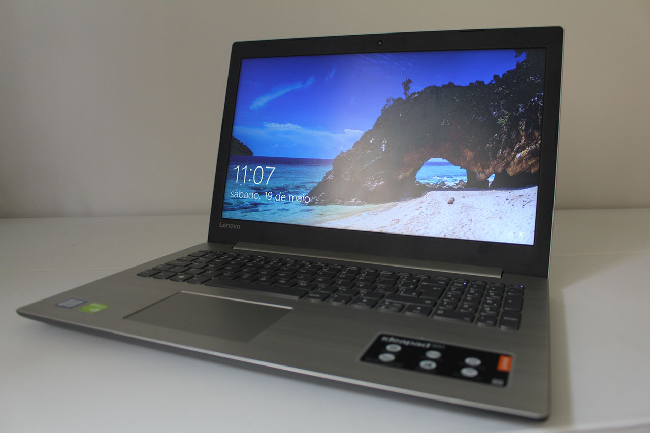 Notebook Lenovo IdeaPad 320 cinza aberto sobre uma mesa, mostrando a tela com papel de parede de paisagem e o teclado numérico.
