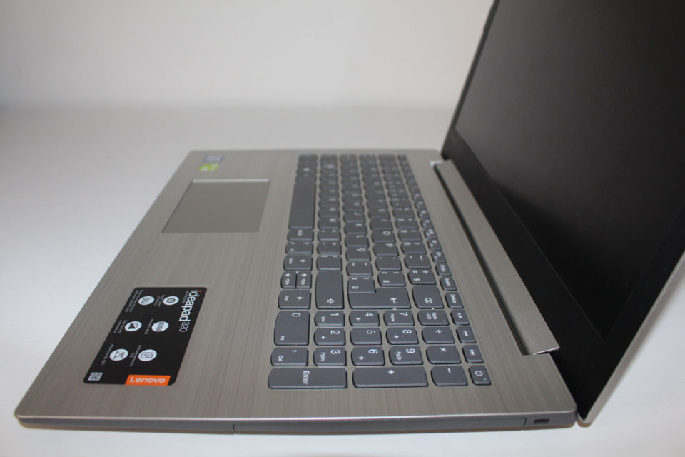 Visão lateral do notebook Lenovo IdeaPad 320 aberto, destacando o acabamento em plástico cinza que imita aço escovado e o teclado numérico.