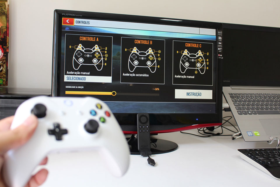 Mão segurando um controle sem fio de Xbox One branco em frente a um monitor de computador que exibe o menu de configuração de controles do Amazon Fire TV Stick.