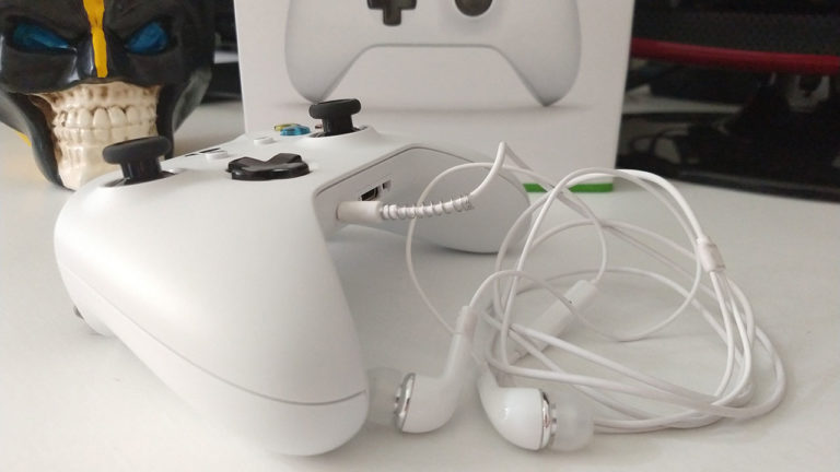 Controle de Xbox One S branco com um fone de ouvido P2 plugado na entrada inferior.
