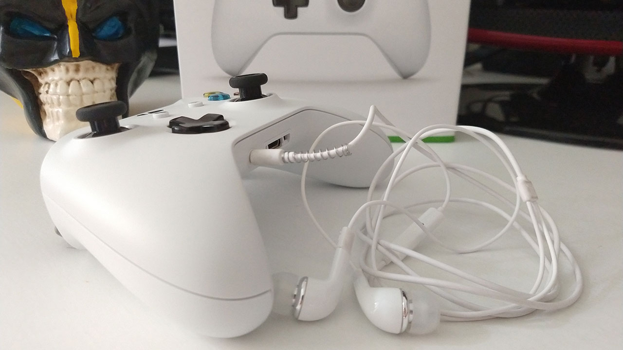 Controle de Xbox One S branco com um fone de ouvido P2 plugado na entrada inferior.