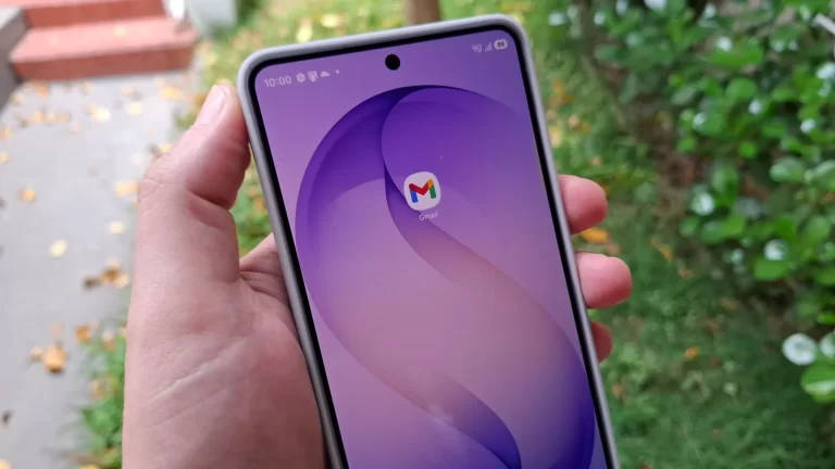 Mão segurando um smartphone que exibe o ícone do Gmail na tela, com um jardim ao fundo, representando o uso do aplicativo móvel para agendamento de e-mails.