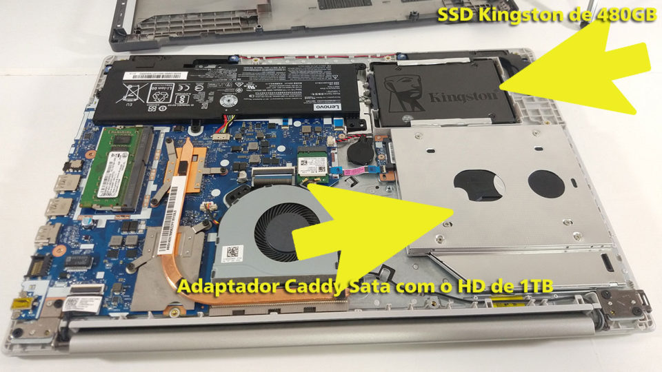 Visão interna do notebook Lenovo IdeaPad 320 com setas amarelas indicando a memória RAM e o adaptador Caddy para o SSD.