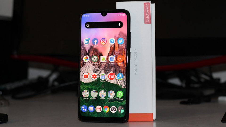 Foto mostrando um smartphone Xiaomi Redmi Note 7 sobre uma mesa, com o texto em destaque "Redmi Note 7: Dicas importantes ANTES de comprar!" e a marca do canal TecnoUp.
