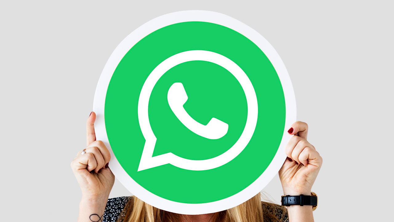 Imagem mostra uma mulher loira segurando a logo do WhatsApp em frente ao seu rosto.