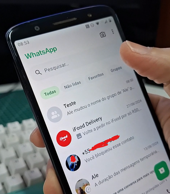 Imagem mostra mão segurando um celular para tocar no filtro grupos do WhatsApp.
