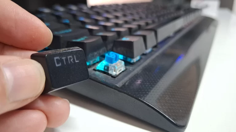 Mão removendo a tecla "CTRL" de um teclado mecânico, revelando o switch de cor azul por baixo.