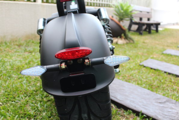 Vista traseira da scooter Bee Green destacando a lanterna de freio e os indicadores de direção (setas).