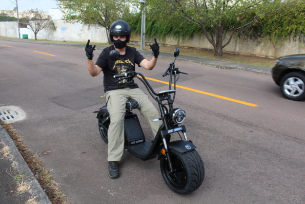 Rapaz pilotando a scooter elétrica Bee Green Sport Plus em uma via urbana, utilizando capacete e luvas de proteção.