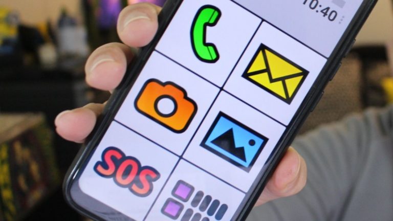 Uma mão segura um smartphone Android exibindo a interface do BIG Launcher, com ícones coloridos e letras grandes para facilitar o uso.