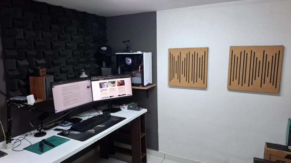 Cenário de estúdio com espumas acústicas pretas na parede e dois painéis difusores Wave de MDF amadeirado instalados ao lado da bancada do computador.