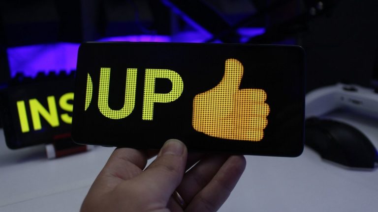 Celular antigo transformado em um letreiro digital de LED exibindo a palavra "UP" com um emoji de positivo.