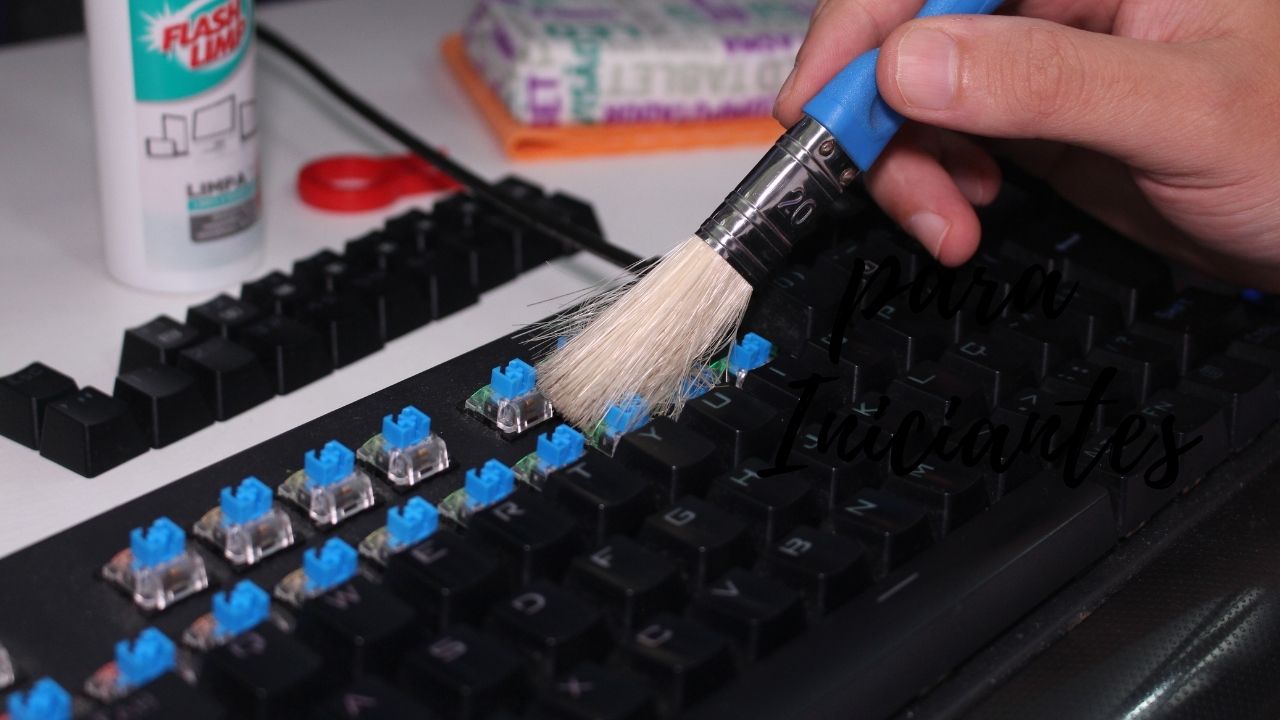 Pessoa utilizando um pincel de cerdas macias para remover poeira entre os switches azuis de um teclado mecânico preto.