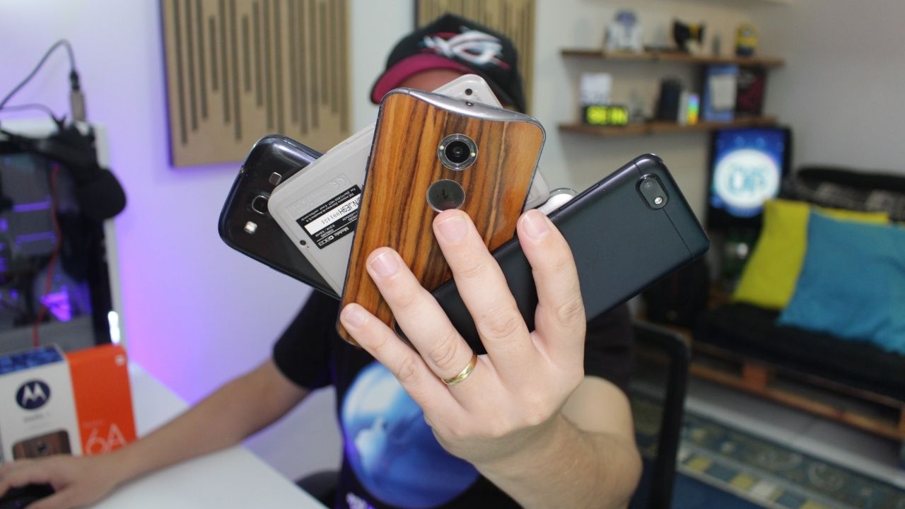 Alexandre, do TecnoUp, segurando vários modelos de smartphones antigos (incluindo um Moto X e um Samsung Galaxy) para ilustrar dicas de reuso de hardware.