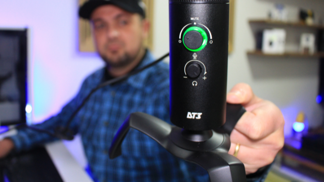 Alexandre Cordeiro segurando o microfone profissional DT3 Boss preto com anel de LED verde ativado em frente a um setup de gravação.