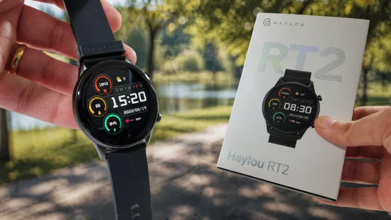 Mão segurando o smartwatch Haylou RT2 ligado ao lado de sua caixa original em um ambiente externo ensolarado.