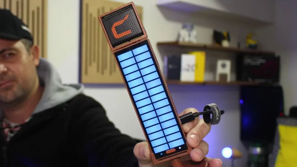 Close no microfone condensador USB Comica Umic sendo segurado por Alexandre do TecnoUp, exibindo o painel de LED RGB e o acabamento que imita madeira.