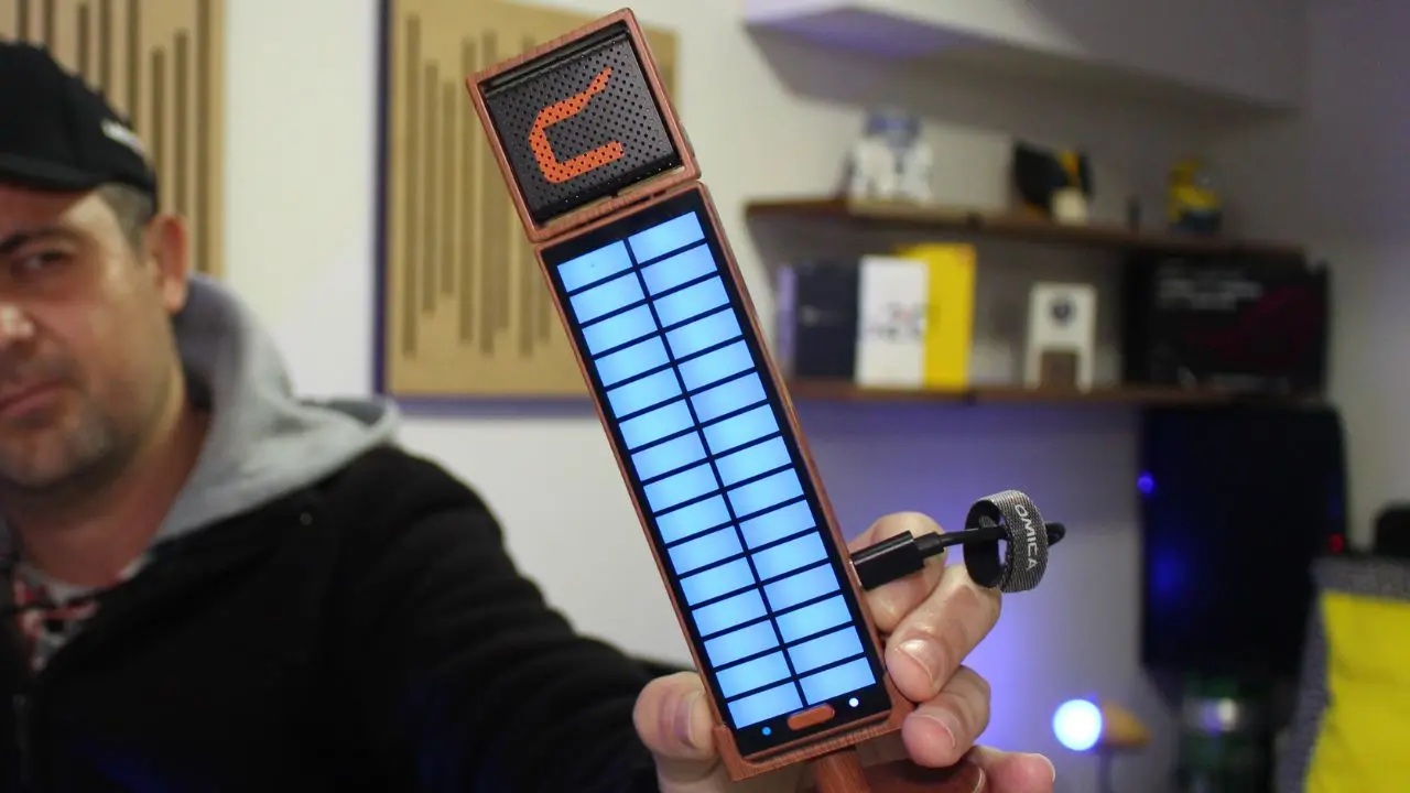 Close no microfone condensador USB Comica Umic sendo segurado por Alexandre do TecnoUp, exibindo o painel de LED RGB e o acabamento que imita madeira.