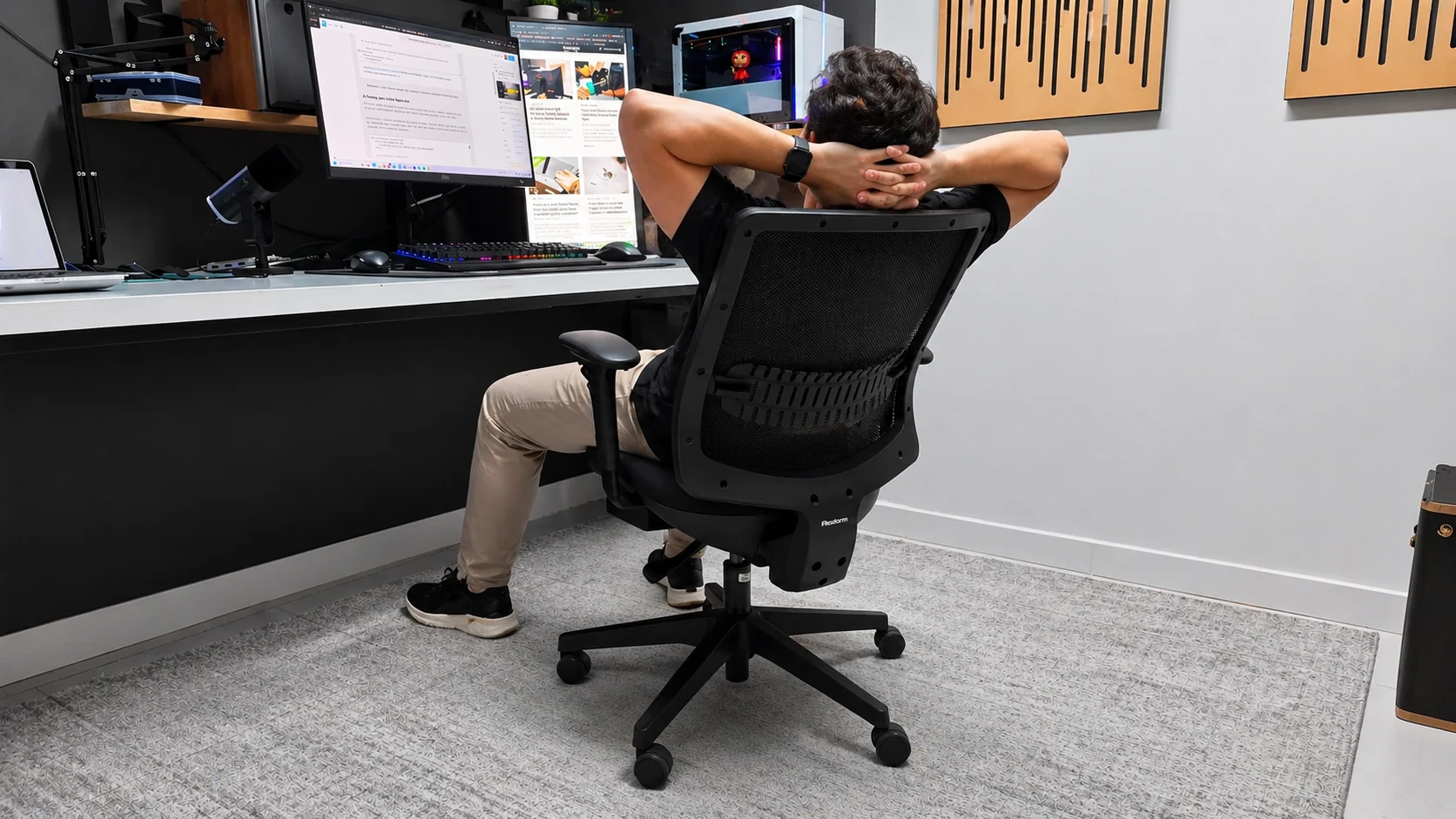 Homem relaxando com as mãos na cabeça sentado na cadeira Flexform Uni All Black em frente a um setup de computador.