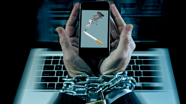 Mãos algemadas a um smartphone com imagem de cigarro aceso na tela.