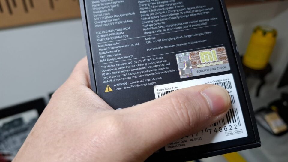 Foto detalhada da traseira da caixa do fone Redmi Buds 3 Pro mostrando o aviso amarelo'WARNING: Cancer and Reproductive Harm' seguido do site P65Warnings.ca.gov.