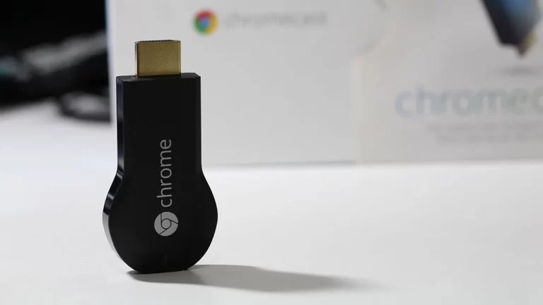 Aparelho Google Chromecast de primeira geração, modelo na cor preta lançado em 2013, deitado sobre uma mesa.