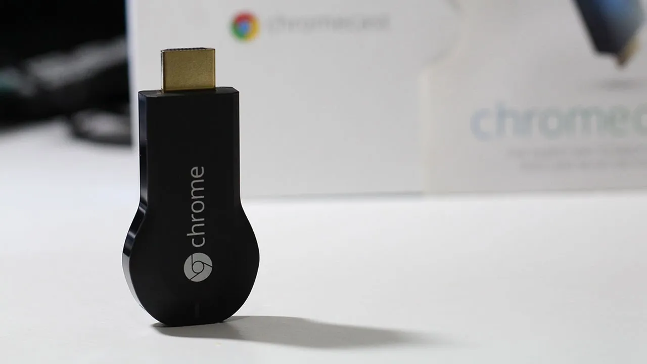 Aparelho Google Chromecast de primeira geração, modelo na cor preta lançado em 2013, deitado sobre uma mesa.