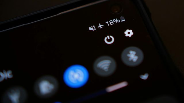 Smartphone sendo segurado no escuro com a interface em Modo Escuro (Dark Mode) ativada, mostrando ícones de Wi-Fi, Bluetooth e texto branco sobre fundo preto