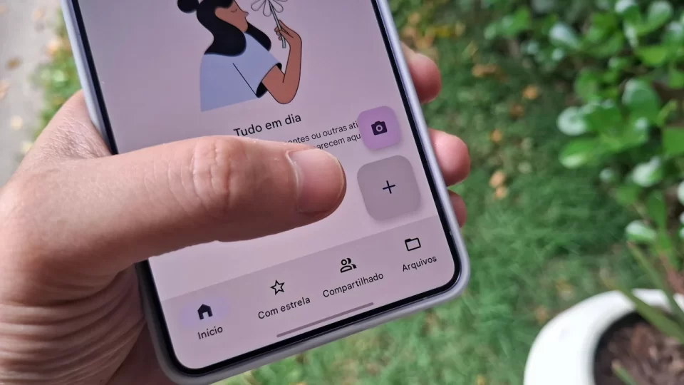 Close em uma mão segurando um smartphone que mostra a interface do aplicativo Google Drive com o menu de criação aberto, destacando a opção "Digitalizar".