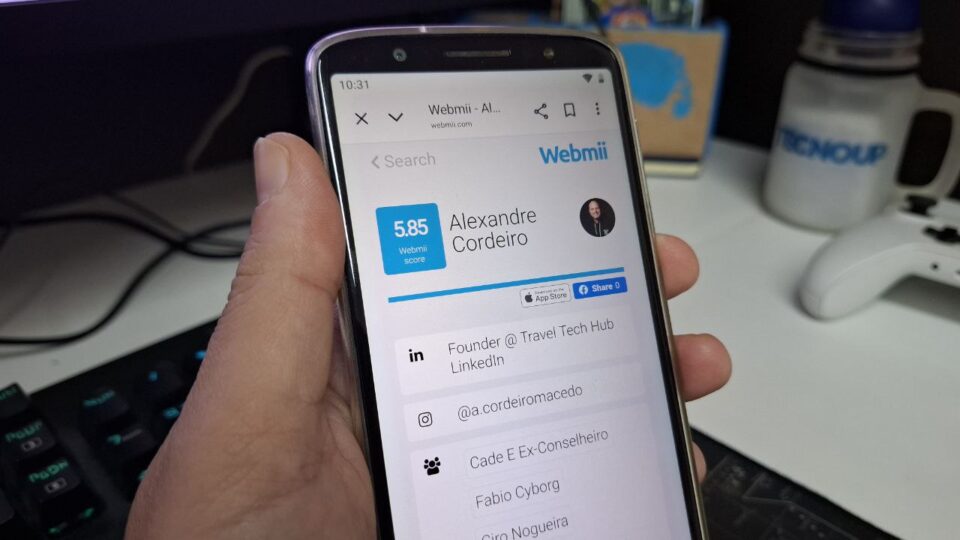 A imagem mostra uma mão segurando celular com o aplicativo Webmii buscando por Alexandre Cordeiro