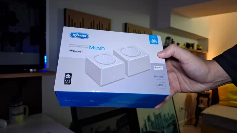 Uma mão segurando a caixa azul e branca do kit de roteador Mesh Knup RW40/MS, com a logo do TecnoUp ao fundo.