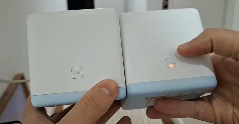 Close nas mãos de um homem segurando dois roteadores Mesh Mercusys Halo S12 brancos, pressionando o botão de pair em um deles.