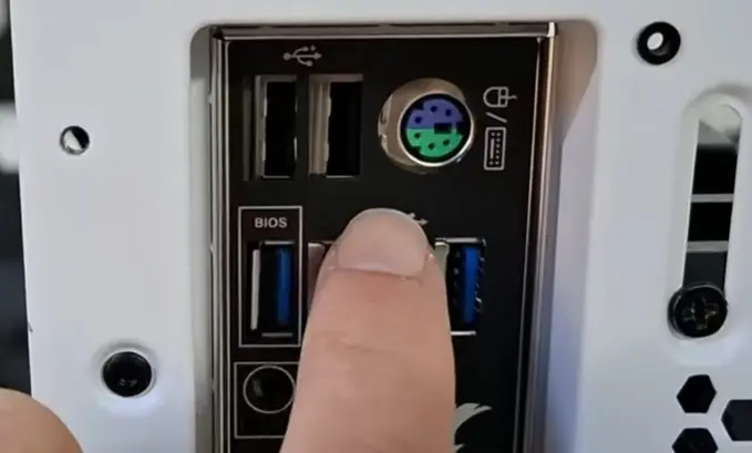 Close do espelho traseiro de uma placa-mãe mal encaixado no gabinete, com um dedo apontando para a falha de alinhamento.