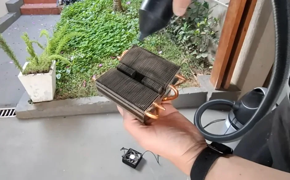 Close-up de técnico realizando a limpeza das aletas de um dissipador Wraith Prism utilizando um soprador de ar portátil em ambiente externo.
