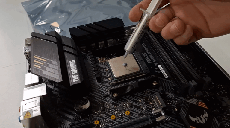 Mão aplicando uma pequena gota de pasta térmica cinza sobre o centro de um processador de computador instalado em uma placa-mãe.