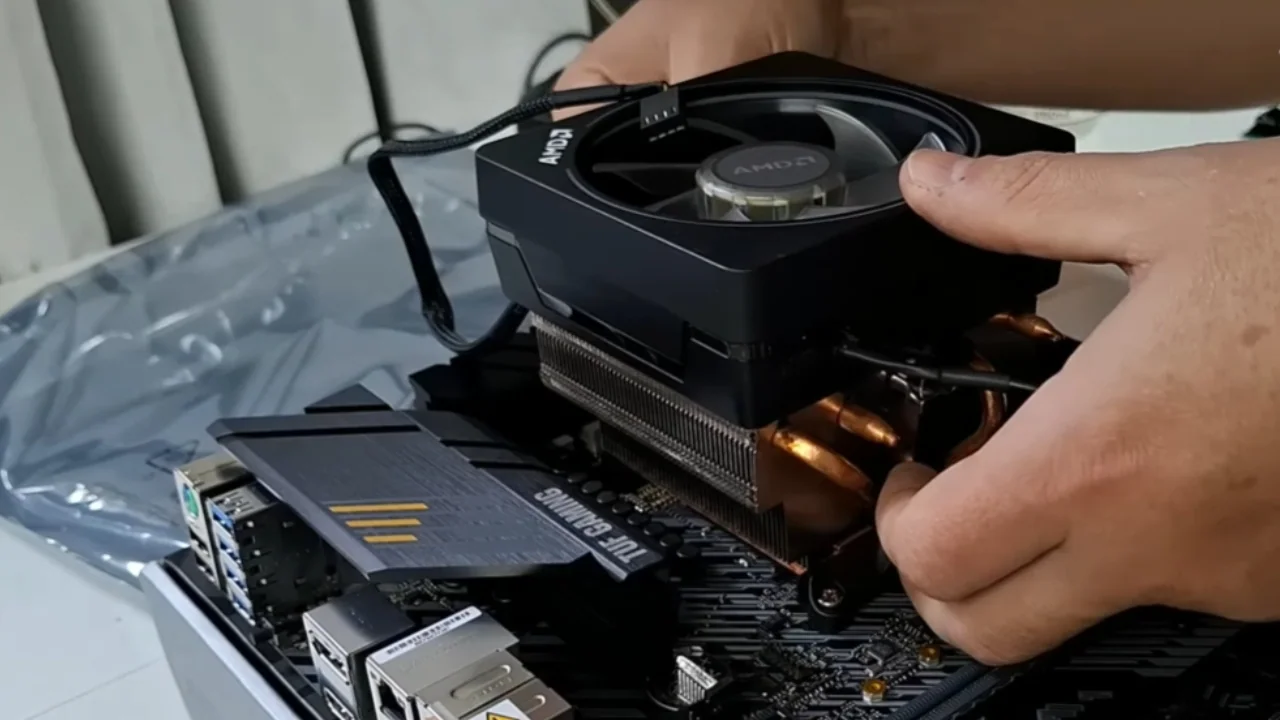 Close-up de mãos realizando a montagem cuidadosa de um computador gamer, instalando um air cooler sobre a placa-mãe em uma bancada de hardware.