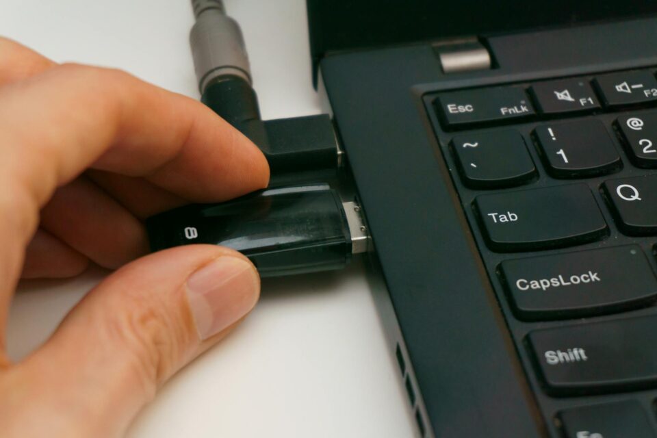 Mão conectando ou removendo um pen drive preto na porta USB lateral de um notebook.