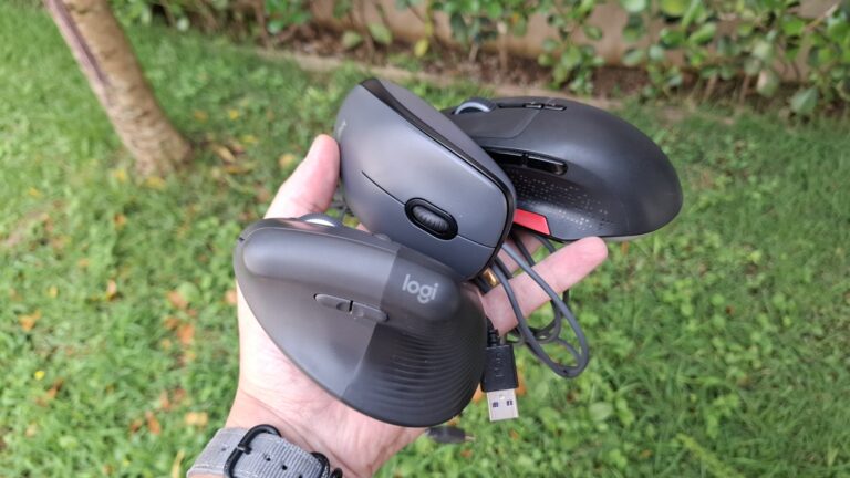 Uma mão segurando três mouses diferentes em um jardim para comparação de tamanho e design