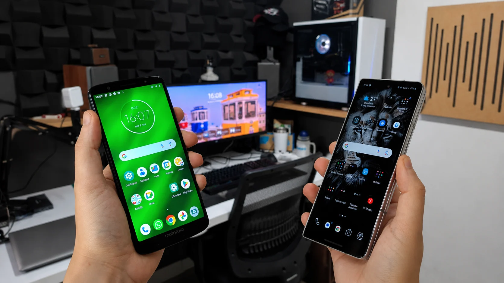 Duas mãos segurando dois smartphones diferentes lado a lado em um escritório com fundo de estúdio focado em tecnologia.