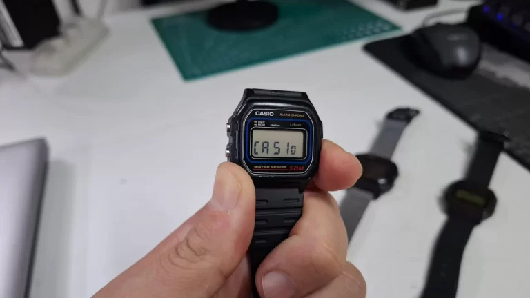 Close em um relógio Casio W-59 exibindo a palavra "CASio" no visor digital após pressionar o botão lateral.