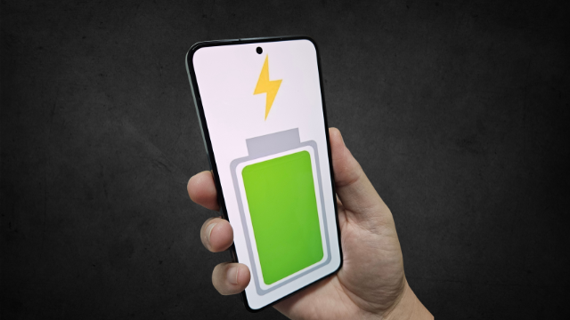Mão segurando um celular Samsung Galaxy com ícone de bateria carregada em verde e um raio de energia, fundo cinza escuro.