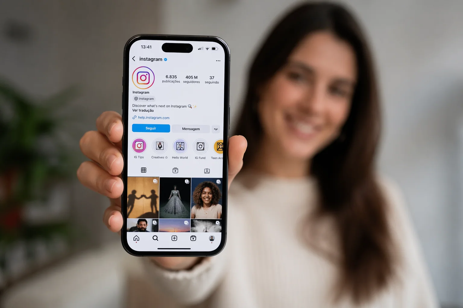 Close de uma mulher sorrindo, segurando um smartphone que exibe a interface do feed do Instagram.