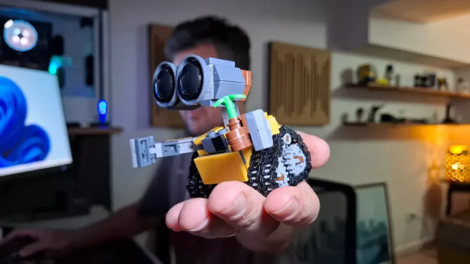 Homem mostrando na mão o mini robô WALL-E montado em frente ao computador no estúdio.